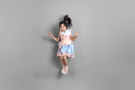 The little cut Asian girl with fancy dressed standing on the grey background.
