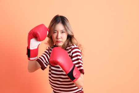 The young Asian woman in casual clothes with gesture of  wearing boxing glove on the orange...