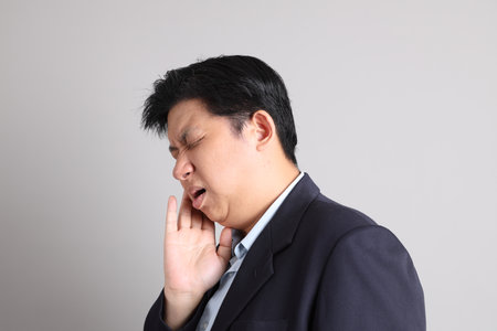 The Asian Businessman with formal dressed with gesture of toothache on the gray background.の写真素材