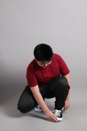 The East Asian kid in the casual clothes with gesture of  wearing shoes on the grey background.