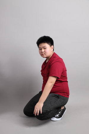 The East Asian kid in the casual clothes with gesture of  Sitting on the grey background.の写真素材