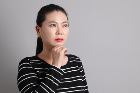 The 40s East Asian woman in the casual clothes with gesture of thinking on the grey background.の写真素材
