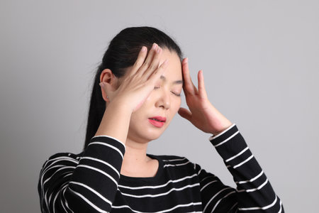 The 40s East Asian woman in the casual clothes with gesture of Headache on the grey background.の写真素材