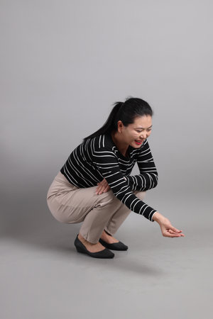 The 40s East Asian woman in the casual clothes with gesture of feeding animal on the grey...