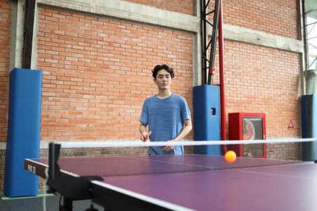 Asian good-looking young man is playing table tennis while holding a ball and a racket in his hands...