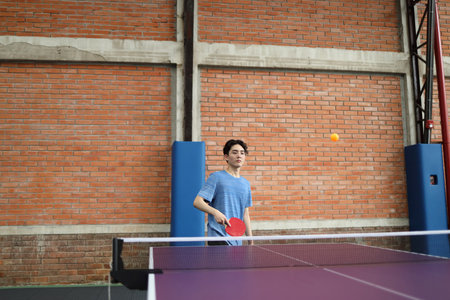 Asian good-looking young man is playing table tennis while holding a ball and a racket in his hands in public table tennis clubの写真素材