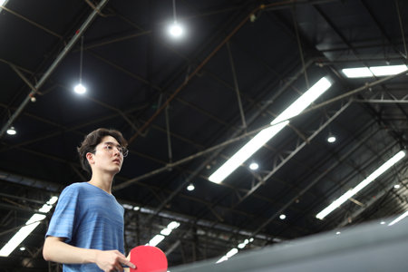 Asian good-looking young man is playing table tennis while holding a ball and a racket in his hands in public table tennis clubの写真素材