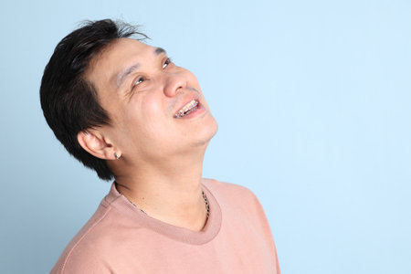 Asian man with braces, wearing a casual t-shirt, gesture of smiling on blue background.の写真素材