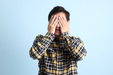Asian man with braces, wearing a casual t-shirt, gesture of Cover eyes on blue background.の写真素材