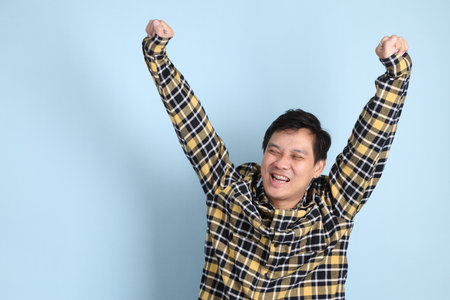 Asian man with braces, wearing a casual t-shirt, gesture of yes, excited, celebrating on blue background.の写真素材