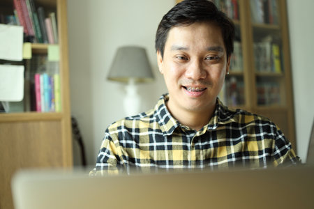 Asian man with braces working on laptop in workspace at home.の写真素材
