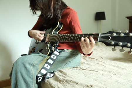 The Southeast Asian girl praticing electric guitar from smart phone.