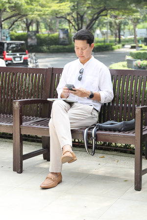 The 40-year-old Asian businessman sitting on the bench, using a smartphone.の写真素材