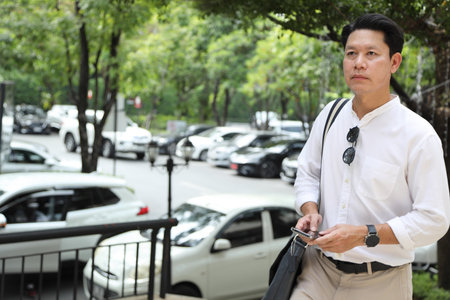 The 40-year-old Asian businessman walking in the parking lot while using a smartphone during the daytime.の写真素材