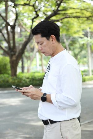 The 40-year-old Asian businessman walking in the parking lot while using a smartphone during the daytime.の写真素材