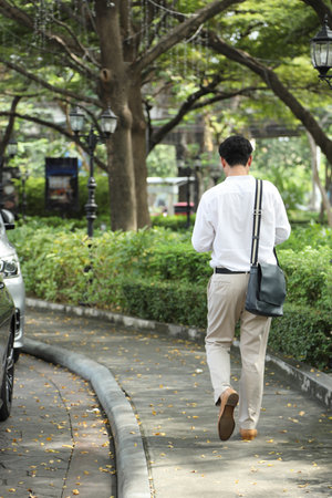 The 40-year-old Asian businessman walking in the parking lot while using a smartphone during the daytime.の写真素材