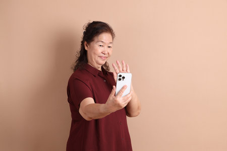 Senior East Asian woman with a deep red shirt standing against a brown background.