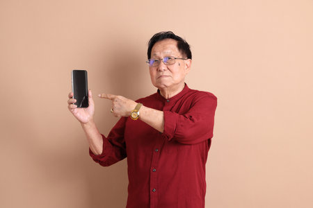 Senior East Asian man with a deep red shirt standing against a brown background.の写真素材
