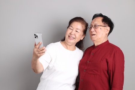 A senior East Asian couple in casual clothes standing against a grey background.の写真素材