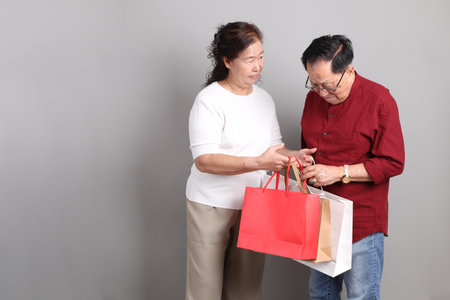 A senior East Asian couple in casual clothes standing against a grey background.の写真素材