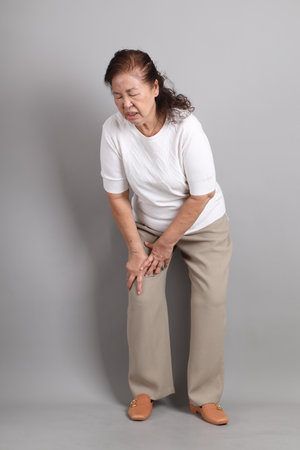 Senior East Asian woman with a white shirt standing against a grey background.の写真素材