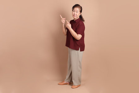 Senior East Asian man with a deep red shirt standing against a brown background.の写真素材