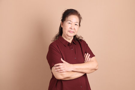 Senior East Asian man with a deep red shirt standing against a brown background.の写真素材