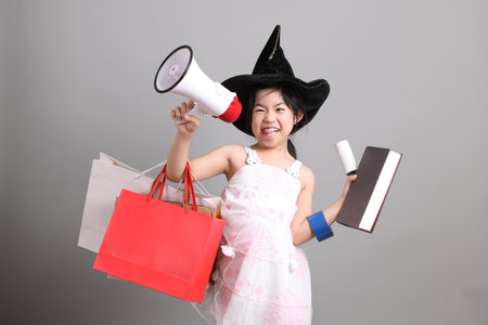An East Asian girl holding many objects, dressed in a crazy outfit, striking a funny pose against a grey background.の写真素材