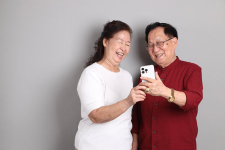 A senior East Asian couple in casual clothes standing against a grey background.の写真素材
