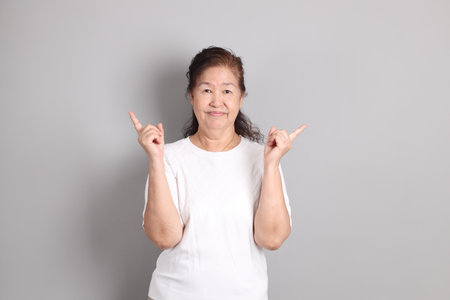 Senior East Asian woman with a white shirt standing against a grey background.の写真素材