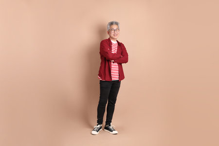 Senior East Asian man with a deep red shirt standing against a brown background.の写真素材