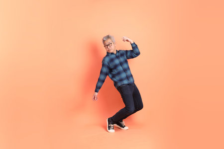A senior East Asian man in a deep blue plaid shirt stands against a peach-pink background.の写真素材