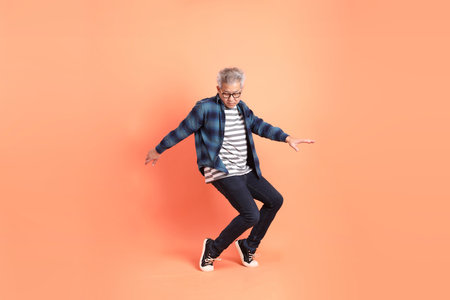 A senior East Asian man in a deep blue plaid shirt stands against a peach-pink background.の写真素材