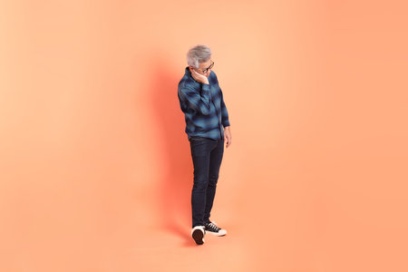 A senior East Asian man in a deep blue plaid shirt stands against a peach-pink background.の写真素材