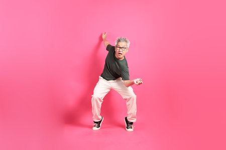 A senior East Asian man stands against a hot pink background, wearing a casual, colorful shirt.の写真素材