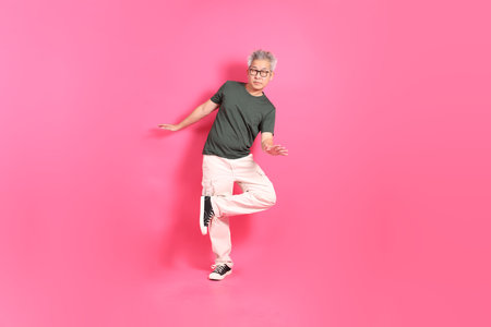 A senior East Asian man stands against a hot pink background, wearing a casual, colorful shirt.の写真素材