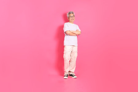 A senior East Asian man stands against a hot pink background, wearing a casual, colorful shirt.の写真素材