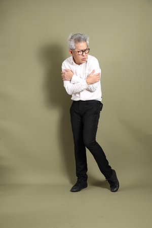 A senior East Asian businessman stands against a dark green backdrop, dressed in a crisp white shirt.の写真素材