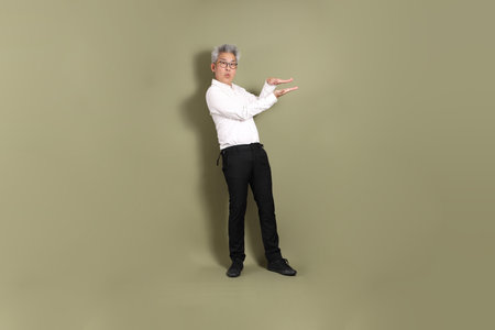 A senior East Asian businessman stands against a dark green backdrop, dressed in a crisp white shirt.の写真素材