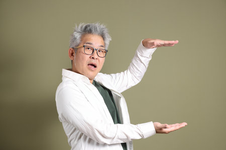 A half-body portrait of an East Asian businessman, isolated against a deep green background, taken in a studio.の写真素材