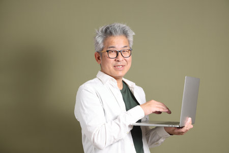 A half-body portrait of an East Asian businessman, isolated against a deep green background, taken in a studio.の写真素材