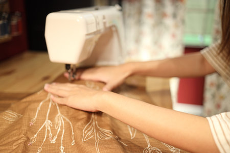 An East Asian woman using a sewing machine to sew clothes at night.