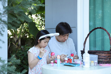 An Asian father helping his daughter paint the eggs for the upcoming Easter.の写真素材