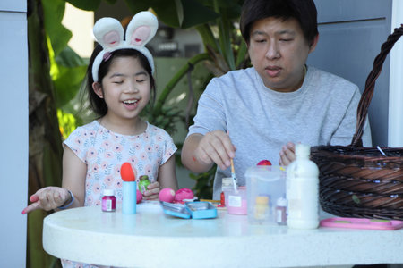 An Asian father helping his daughter paint the eggs for the upcoming Easter.