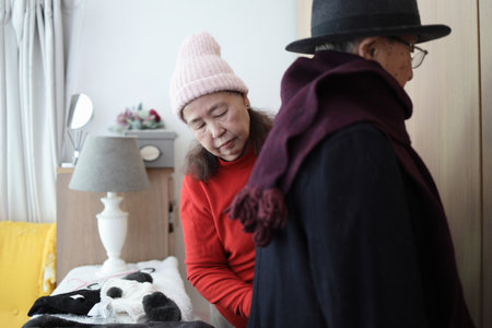 An East Asian elderly couple helping each other dress in winter clothes to go outside