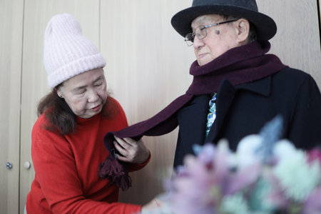 An East Asian elderly couple helping each other dress in winter clothes to go outside