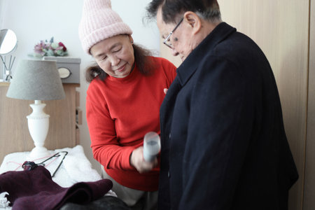 An East Asian elderly couple helping each other dress in winter clothes to go outsideの写真素材