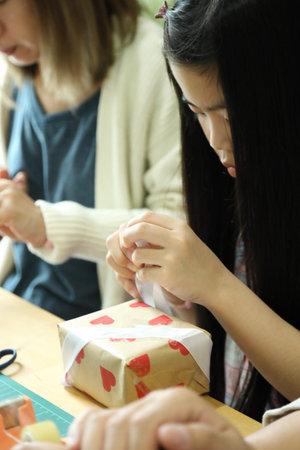 East Asian parents helping their daughter and teaching her how to wrap a present for the upcoming...