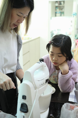 The East Asian mother is baking and decorating the house bread with help from her daughter for the...
