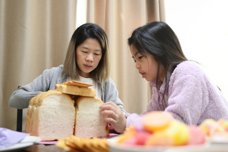 The East Asian mother is baking and decorating the house bread with help from her daughter for the upcoming party.の写真素材